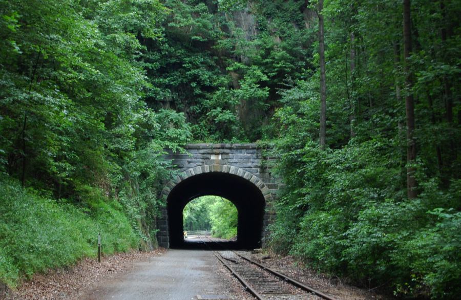 Railroad tracks run through a stone bridge in the woods.