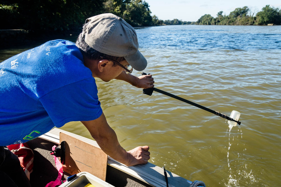 A man uses a long-handled grabber to dip a plastic bottle in and out of a river, as part of his work to take a water quality sample.