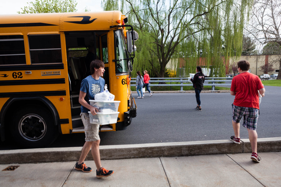 Student gets off bus holding a box of supplies.