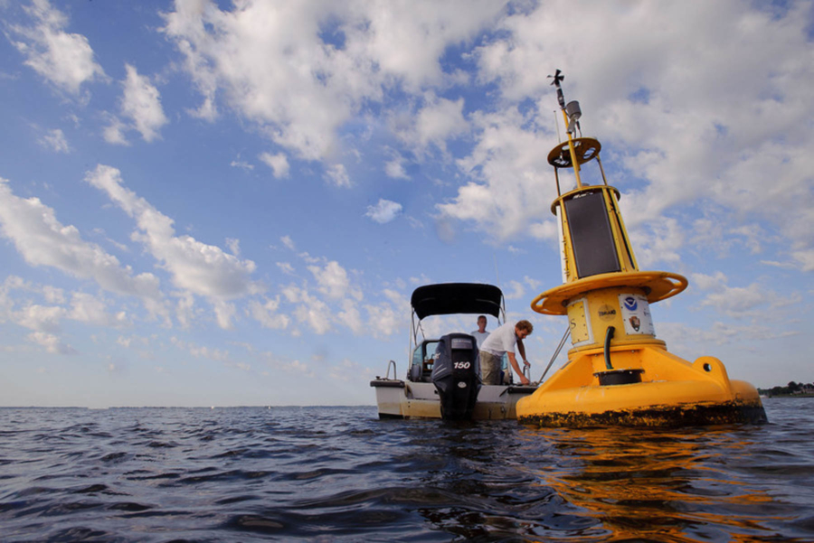 A large yellow monitoring buoy looms in front of the small research boat.