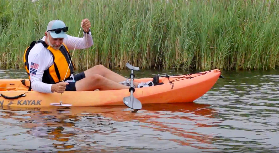 Volunteer in a kayak drops Secchi disc into the water.